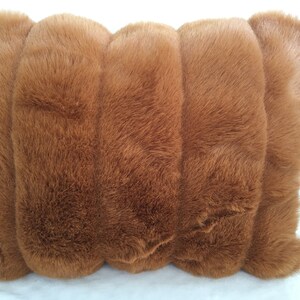 May include: A rectangular, plush pillow in a warm brown hue. The pillow's surface is covered in soft, faux fur, creating a textured appearance. The design features a series of rounded, vertical sections, adding visual interest. The pillow is designed for comfort and decorative use.