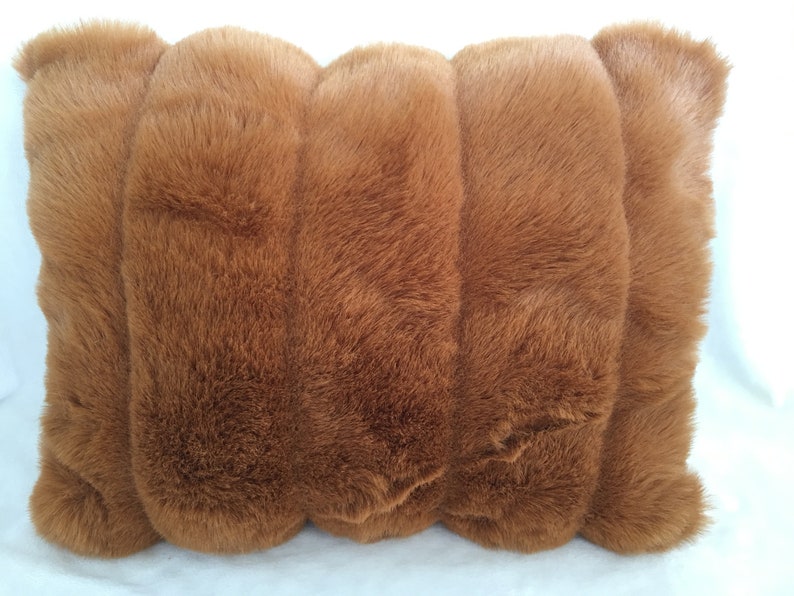 May include: A rectangular, plush pillow in a warm brown hue. The pillow's surface is covered in soft, faux fur, creating a textured appearance. The design features a series of rounded, vertical sections, adding visual interest. The pillow is designed for comfort and decorative use.