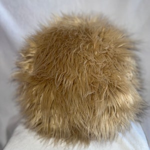 May include: A round, fluffy, tan-colored throw pillow with a soft, shaggy texture.