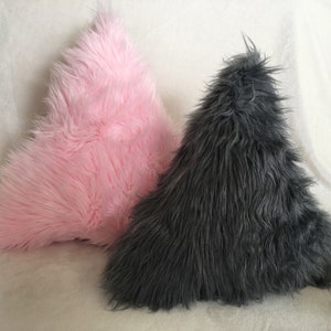 May include: Two triangular-shaped decorative pillows. One is a soft pink color, and the other is a dark gray. Both pillows have a long, shaggy fur texture, creating a cozy and inviting appearance.