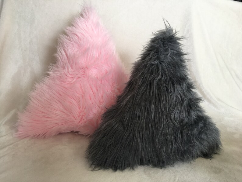 May include: Two triangular-shaped decorative pillows. One is a soft pink color, and the other is a dark gray. Both pillows have a long, shaggy fur texture, creating a cozy and inviting appearance.
