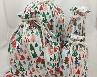 May include: A set of four drawstring bags in varying sizes. The bags are white with a repeating pattern of colorful Christmas trees in red, green, and pink. Each bag has a natural-colored drawstring closure.
