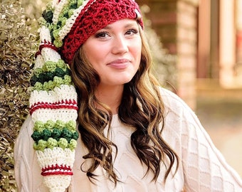 May include: A white, red, and green crocheted elf hat with a pom-pom on the end. The hat has a striped pattern and is decorated with green and white bobbles.