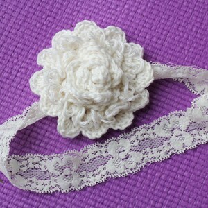 May include: A white crocheted flower headband with a lace trim. The headband is on a purple background.