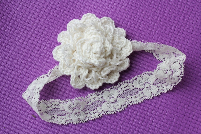 May include: A white crocheted flower headband with a lace trim. The headband is on a purple background.