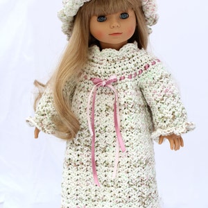 May include: A doll wearing a crocheted nightgown with pink ribbon accents and a matching crocheted hat. The doll has long blonde hair and blue eyes.