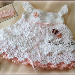 Pu&ograve; includere: Abito da neonata bianco all'uncinetto con un nastro rosa e un bordo in crochet rosa. L'abito &egrave; decorato con tre farfalle all'uncinetto rosa, marrone e bianco.