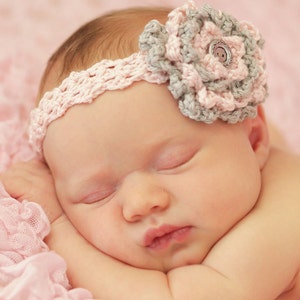 May include: A sleeping baby wearing a pink and gray crocheted headband with a flower detail and a silver button.