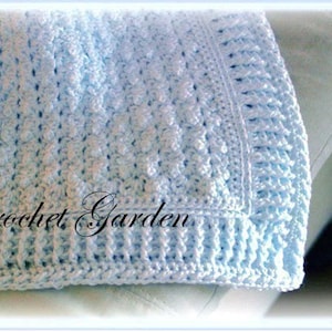 May include: A light blue crocheted baby blanket with a textured stitch pattern. The blanket has a border of single crochet stitches. The text "Crochet Garden" is visible in the lower left corner of the blanket.