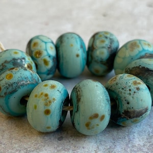 May include: A strand of turquoise blue glass beads with brown and gold speckles. The beads are round and have a slightly irregular shape.