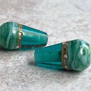 May include: Two teal blue glass beads with white and green marbling and a gold band around the centre.