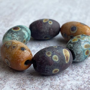 May include: A strand of seven oval-shaped glass beads with a mottled pattern of brown, blue, and yellow. The beads are strung on a black cord.
