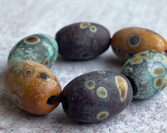 May include: A strand of seven oval-shaped glass beads with a mottled pattern of brown, blue, and yellow. The beads are strung on a black cord.