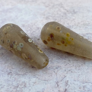 May include: Two brown glass beads with a speckled pattern of white, yellow, and brown spots.