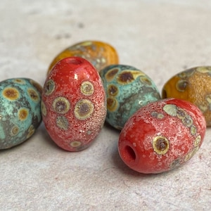 May include: Five oval-shaped glass beads with a speckled pattern in shades of red, orange, and blue.