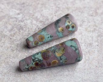 May include: Two purple, green, and gold cone-shaped glass beads with a speckled pattern.