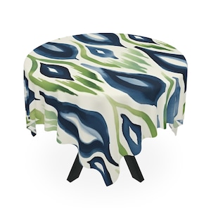 May include: Round tablecloth with a blue and green abstract pattern. The tablecloth is draped over a table with black legs.