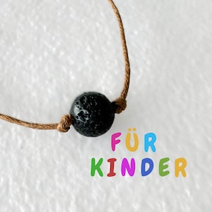 Könnte beinhalten: Eine braune Schnurkette mit einer schwarzen Lavasteinkugel. Der Text "FÜR KINDER" ist unterhalb der Kette in bunten Buchstaben geschrieben.