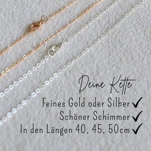 May include: Two delicate chains, one gold and one silver, lie on a textured surface. The chains are shown in different lengths, with checkmarks indicating available sizes: 40, 45, and 50 centimetres. The text "Deine Kette" is written in cursive above the chains.