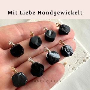 May include: Eight black gemstone pendants wrapped in silver wire with gold accents. The pendants are displayed on a hand.