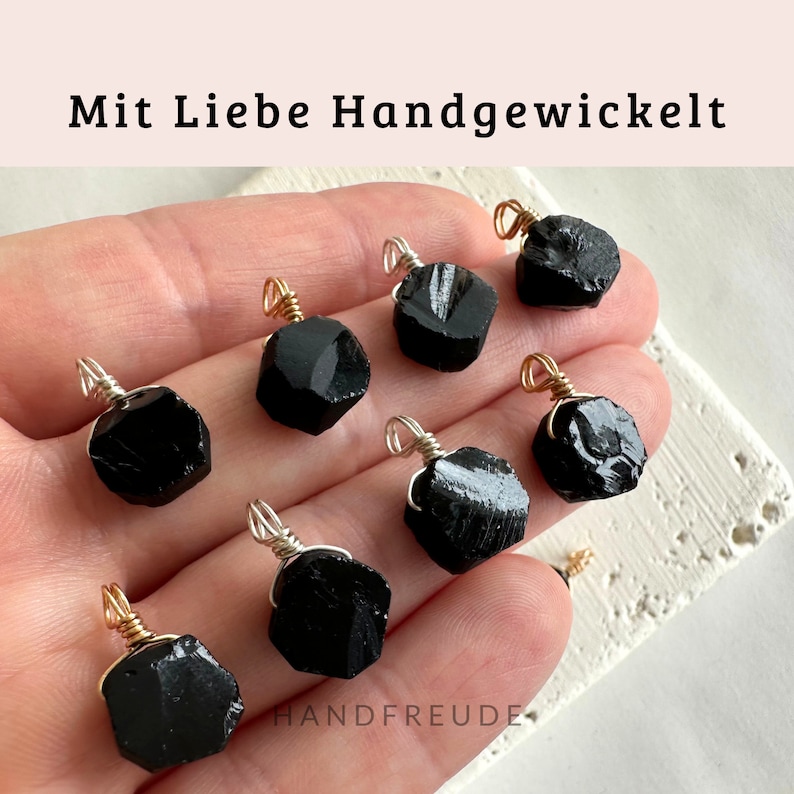 May include: Eight black gemstone pendants wrapped in silver wire with gold accents. The pendants are displayed on a hand.