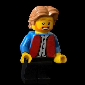Puede incluir: Una minifigura de Lego con pelo marrón, una chaqueta azul, un chaleco rojo y una cara amarilla con una sonrisa.