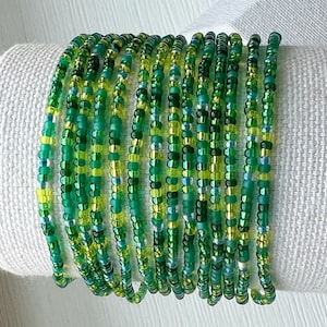 May include: A stack of green and yellow beaded bracelets. The beads are small and have a slight iridescent sheen.