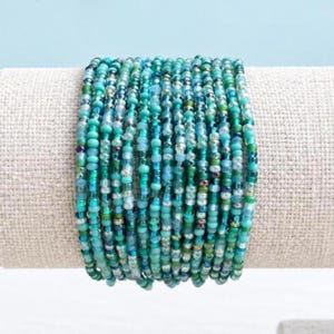 May include: A multi-strand bracelet composed of numerous small, round glass beads in various shades of turquoise, teal, aqua, and light blue. The beads are arranged in multiple parallel rows, creating a dense, textured appearance with a glossy finish.