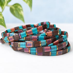 May include: A multi-strand bracelet composed of rectangular beads in alternating colors of turquoise blue, metallic copper, and matte dark brown. The beads are arranged in a repeating pattern, creating a layered, stacked appearance with a smooth finish.