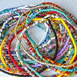 May include: A collection of multiple strands of small, colorful glass seed beads arranged in a circular pattern. The beads feature a wide variety of vibrant colors including red, yellow, blue, green, white, black, orange, and metallic gold tones.
