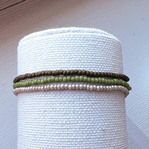 May include: Three layered bracelets made of small beads. The top layer is brown, the middle layer is green, and the bottom layer is silver.
