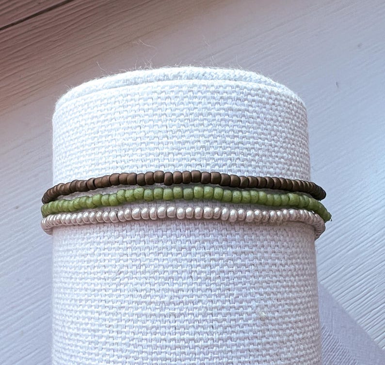 May include: Three layered bracelets made of small beads. The top layer is brown, the middle layer is green, and the bottom layer is silver.