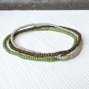 May include: Three layered bracelets made of small beads in shades of green, brown, and white.