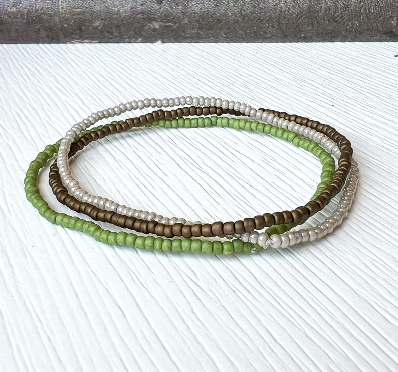 May include: Three layered bracelets made of small beads in shades of green, brown, and white.