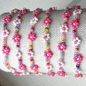 May include: Six beaded bracelets with a floral design. Each bracelet features pink flower beads interspersed with smaller, colorful beads. The bracelets are displayed on a white surface, showcasing the intricate details and vibrant colors of the jewelry.