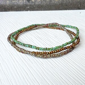 May include: Three layered beaded bracelets in shades of green, gold, and brown. The bracelets are made of small, round beads.
