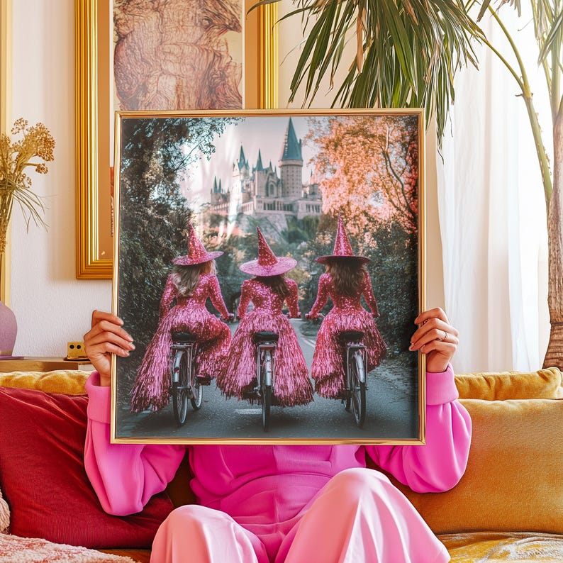 May include: Three women dressed in pink sequined witch costumes ride bicycles in front of a castle. The women are wearing pointy hats and have their backs to the camera. The castle is in the background and is surrounded by trees.