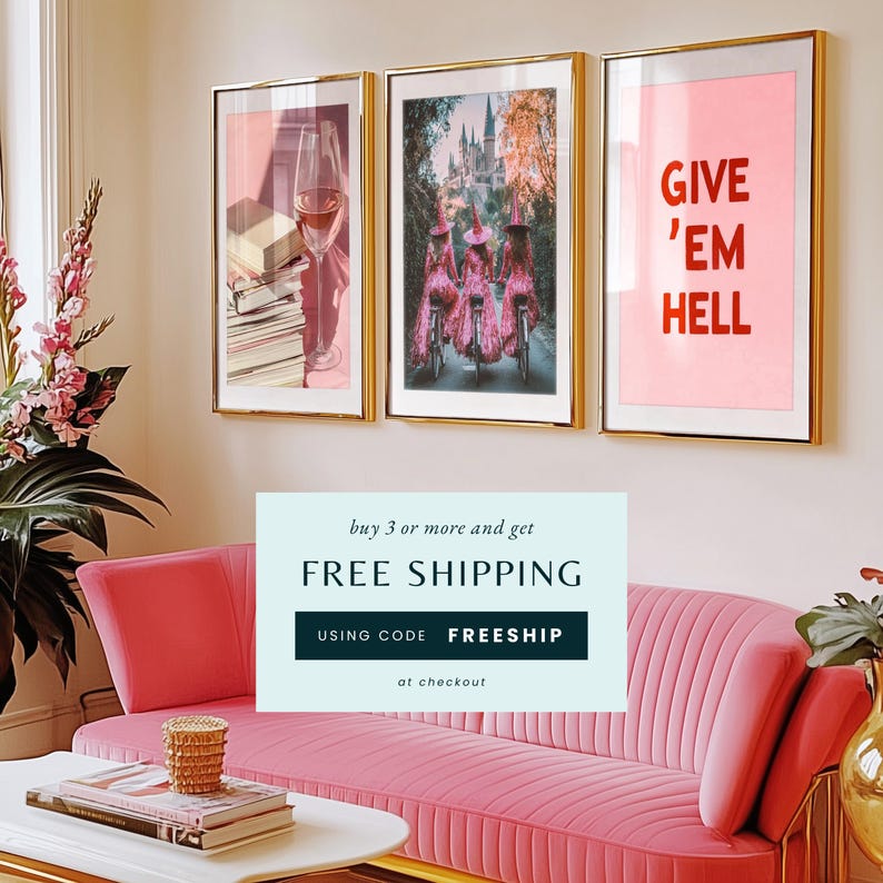 May include: Three framed art prints with pink backgrounds. The left print features a glass of wine and a stack of books. The centre print shows three women in pink dresses riding bicycles in front of a castle. The right print has the text "GIVE 'EM HELL" in red letters. A pink sofa is in the foreground with a free shipping offer displayed in front of it.