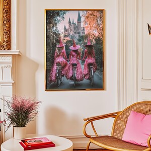 May include: Three women dressed in pink, sparkly dresses and witch hats ride bicycles in front of a castle. The castle is a light grey colour with tall towers and a pointed roof. The women are riding away from the viewer, and the castle is in the background.