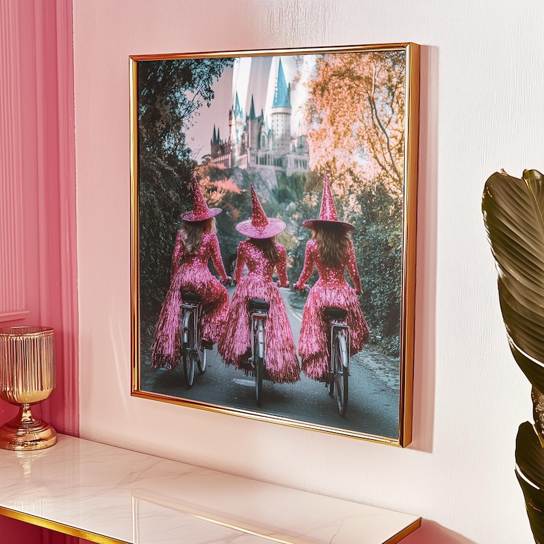 framed photo of three witches dressed in sparkly pink outfits riding bikes to a large castle on a hill