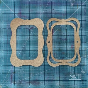 May include: Two gold glitter frames with scalloped edges. The larger frame is layered on top of a smaller frame. Both frames are on a blue cutting mat.