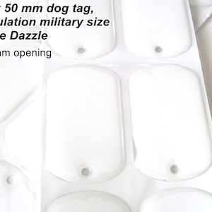 May include: A sheet of blank, white dog tags. Each tag is rectangular with rounded corners and a small hole for attachment. The text "30 x 50 mm dog tag, regulation military size Dixie Dazzle 3mm opening" is visible.