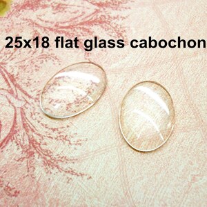 May include: Two clear glass cabochons, each measuring 25x18 mm, are shown on a pink and white patterned surface.