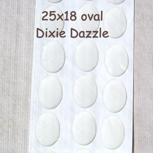 May include: A sheet of oval-shaped, white embellishments. The text "25x18 oval Dixie Dazzle" is printed at the top. The embellishments are arranged in rows and columns on a white background.