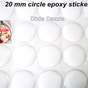 May include: A sheet of clear, 20 mm circle epoxy stickers. The image includes a pendant with a floral and bird design. The text "20 mm circle epoxy sticker" and "Dixie Dazzle" are visible.