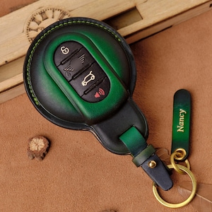 Può includere: Portachiavi per auto in pelle verde e nera con portachiavi abbinato. Il portachiavi ha pulsanti per bloccare, sbloccare e altre funzioni dell'auto. Il portachiavi è inciso con il nome "Nancy" in lettere dorate.
