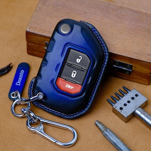 May include: A blue leather key fob cover with a silver keyring. The key fob has black buttons with white icons and a red button. The word "Doanto" is printed on a blue tag attached to the keyring. A wooden box and tools are in the background.