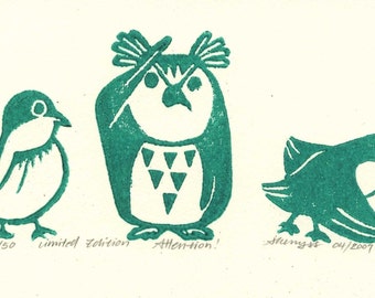 May include: A green linocut print of three birds. The leftmost bird is a small, round bird with a large eye. The middle bird is an owl with a large eye and a triangular pattern on its chest. The rightmost bird is a small bird with a large eye and a wing outstretched. The print is numbered 10/50 and says "limited edition" and "Attention!"