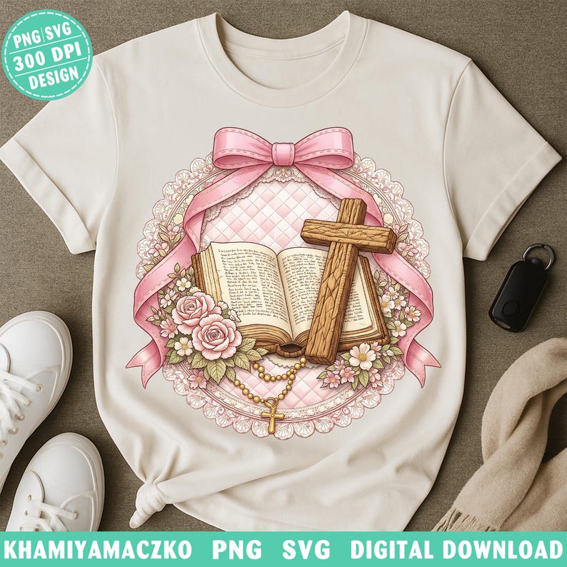 May include: Cream-colored t-shirt featuring a detailed graphic of a wooden cross, open book, pink ribbon, and floral elements. The design includes the text "PNG SVG 300 DPI DESIGN" at the top left. The bottom of the shirt has the text "KHAMIYAMACZKO PNG SVG DIGITAL DOWNLOAD".