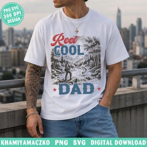 May include: White t-shirt with a graphic design featuring the text "Reel Cool Dad" in red and blue, with a fishing scene illustration. The design includes a fisherman, a fish, and a river scene.
